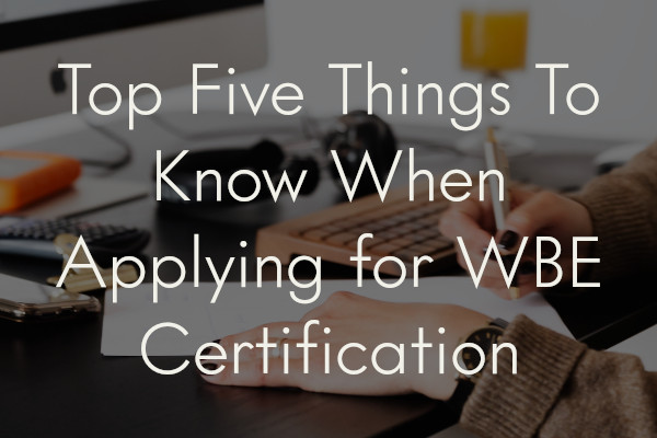 A woman's hand signing a contract, overlaid with the title of the article.: Top Five Things To Know when Applying For WBE Certification