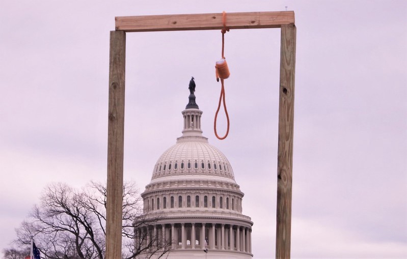 The wooden frame of a gallows with noose constructed by Capitol rioters, framing the cupola of the U.S. Capitol building. (Blog Post: "Employment At Will" in Illinois)