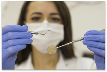 A white woman in a dentist's mask with blue disposable gloves, working attentively with dentist's tools.