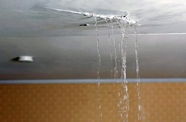 A closeup of a crack in a white ceiling. It's leaking rather badly, with several streams of water trickling into the room below.