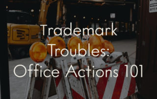 A picture of red and white striped roadblocks stacked against each other, overlaid with the title of the blog post: "Trademark Troubles: Office Actions 101"
