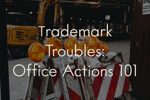 A picture of red and white striped roadblocks stacked against each other, overlaid with the title of the blog post: "Trademark Troubles: Office Actions 101"